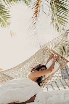 A serene moment of relaxation as a woman enjoys the breeze in a hammock under palm trees.