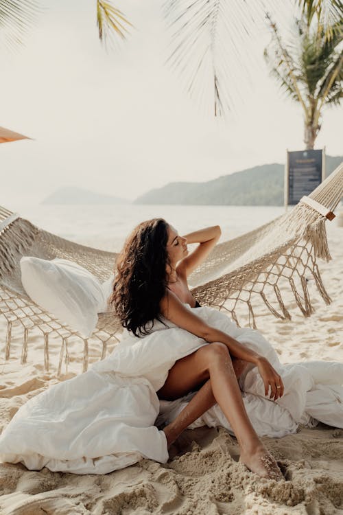 白色礼服的妇女坐在海滩的白色纺织品