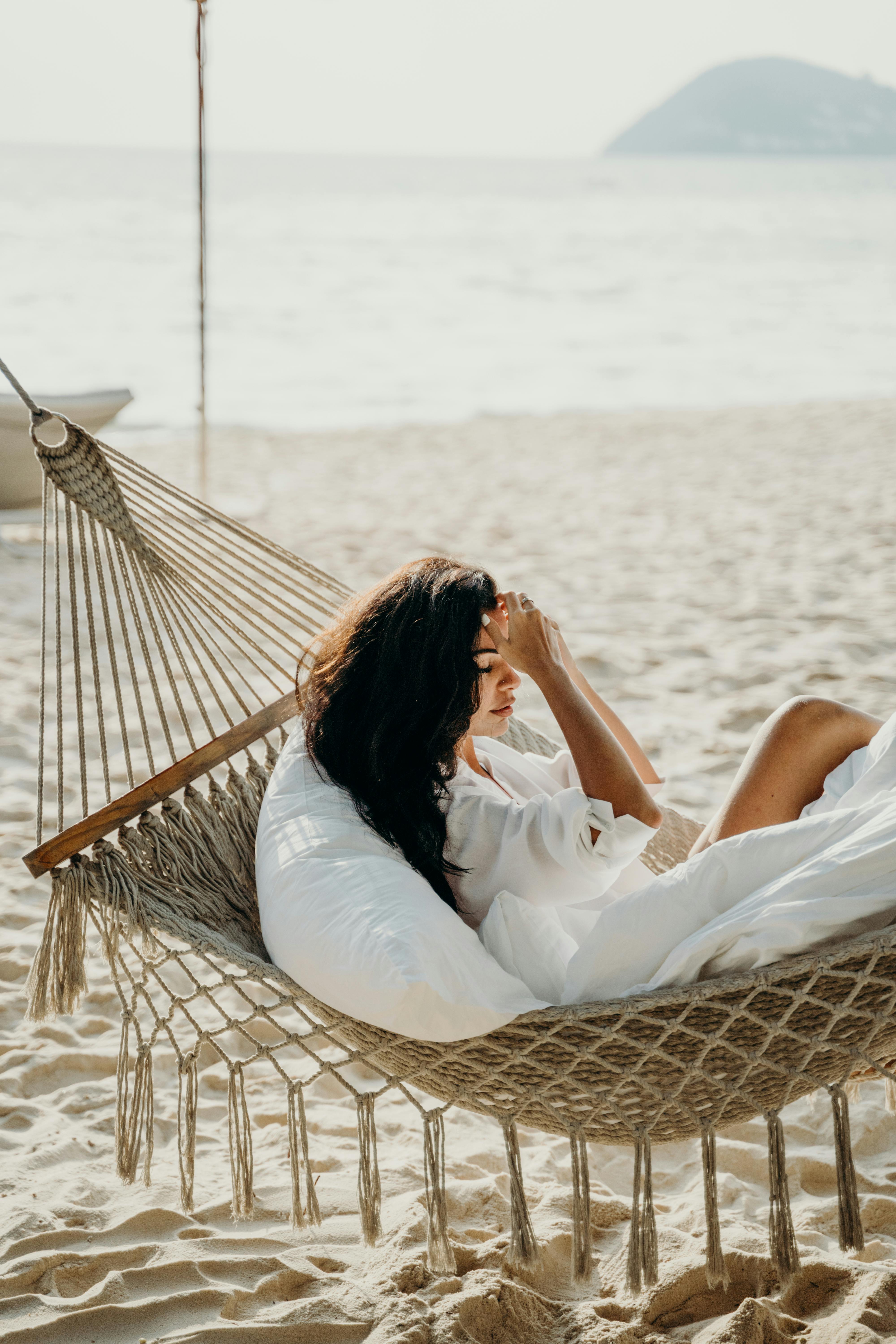 宁静的女人躺在阳光明媚的巴厘岛海滩的吊床上，享受着夏日的时光
