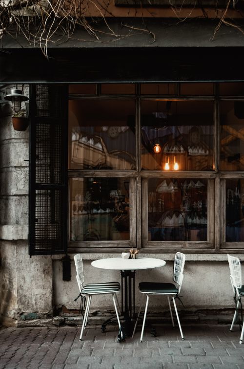 Free Table and chairs on tiled pavement near aged cafeteria building exterior with shiny lamps in town Stock Photo