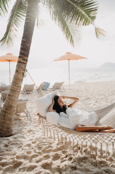 A woman enjoying a sunny day in a hammock on a Bali beach with palm trees and ocean views.