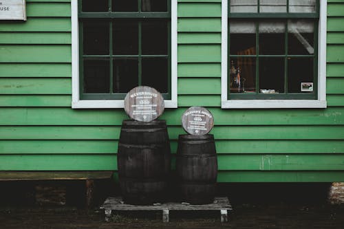 Wooden barrels on shabby wooden platform standing near green wall of small house