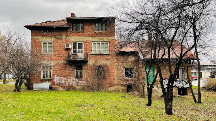 An Old Brick House Surrounded By Deciduous Trees