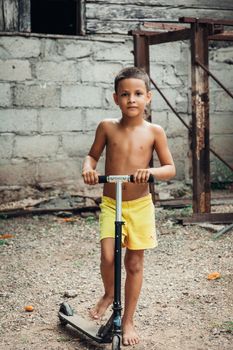 A shirtless young boy on a kick scooter in an outdoor setting.