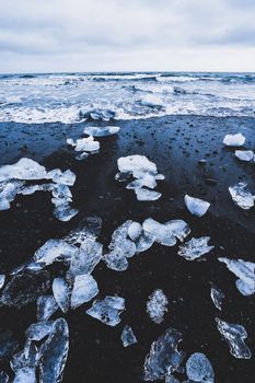 From above rough rocky coast with dark sand and big ice chunks at nordic picturesque seascape on cold cloudy day