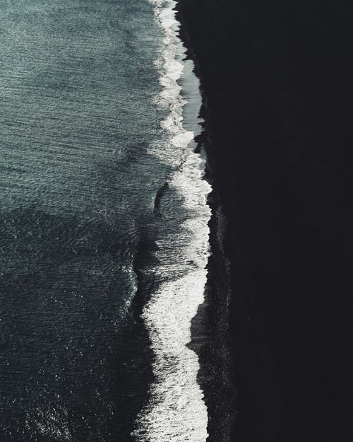 Free Drone view of foamy ocean water rolling on dark sand beach in daylight Stock Photo