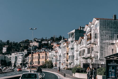 Free Asphalt driveway with cars riding along residential houses located on roadside against blue sky on street with people on bus stop in city Stock Photo