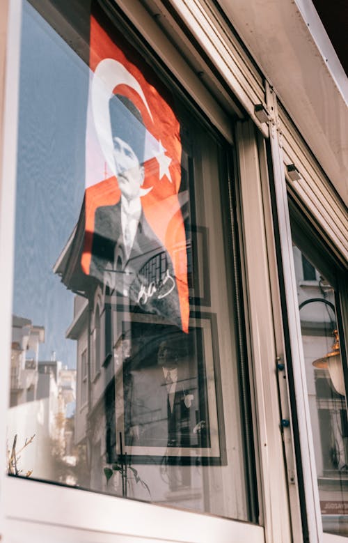 From below image of Turkish president Mustafa Kemal Ataturk hanging on glass on reflected window of building in city on street
