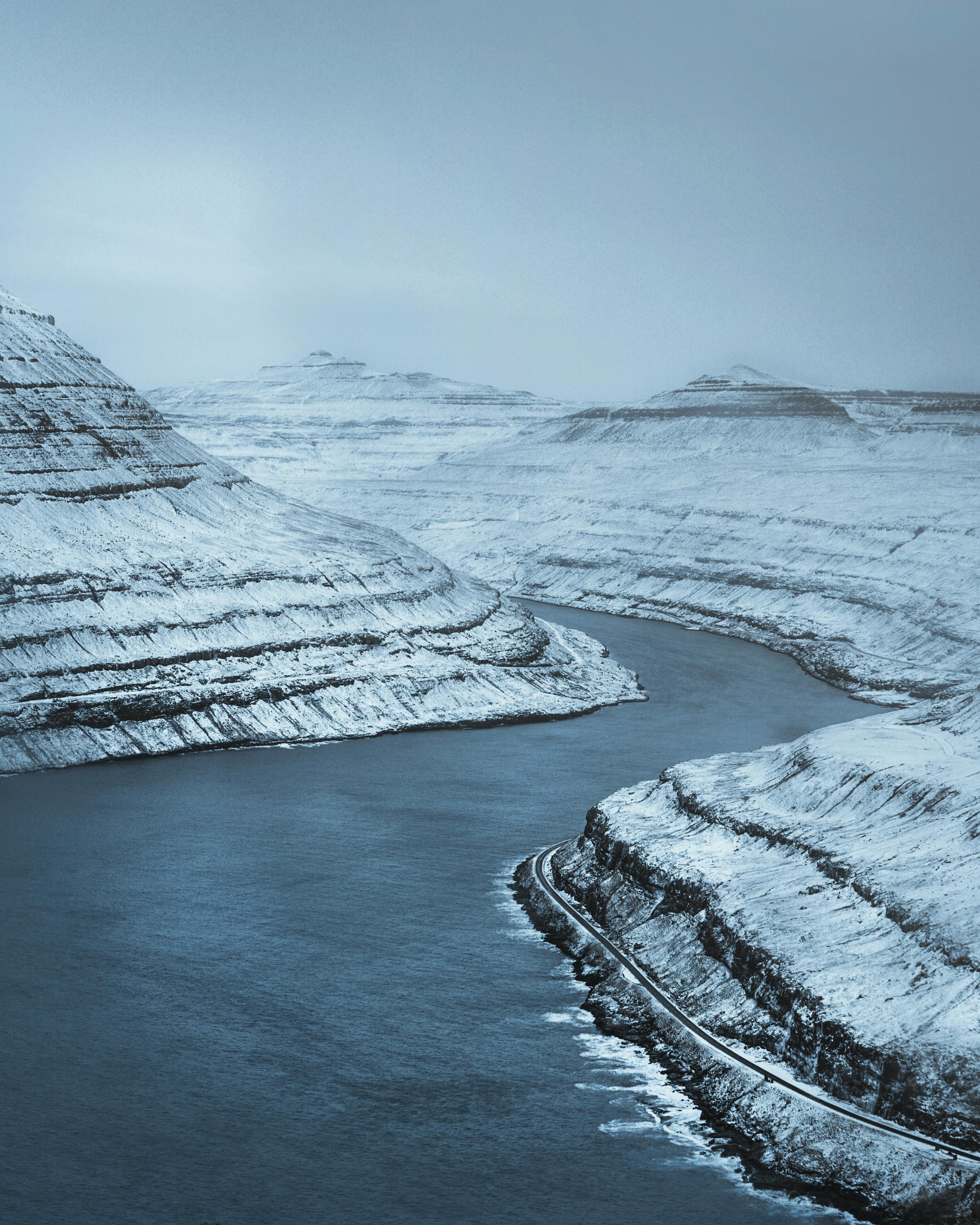 From above of frozen river flowing in mountainous terrain against cloudless blue sky