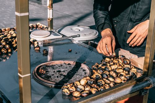 Free Anonymous professional male cook standing at metal counter with pan while roasting piles of tasty chestnuts on sunny street in city Stock Photo