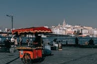 Red food truck located on crowded quay near sea against coastal city with buildings and Galata tower in Istanbul in Turkey