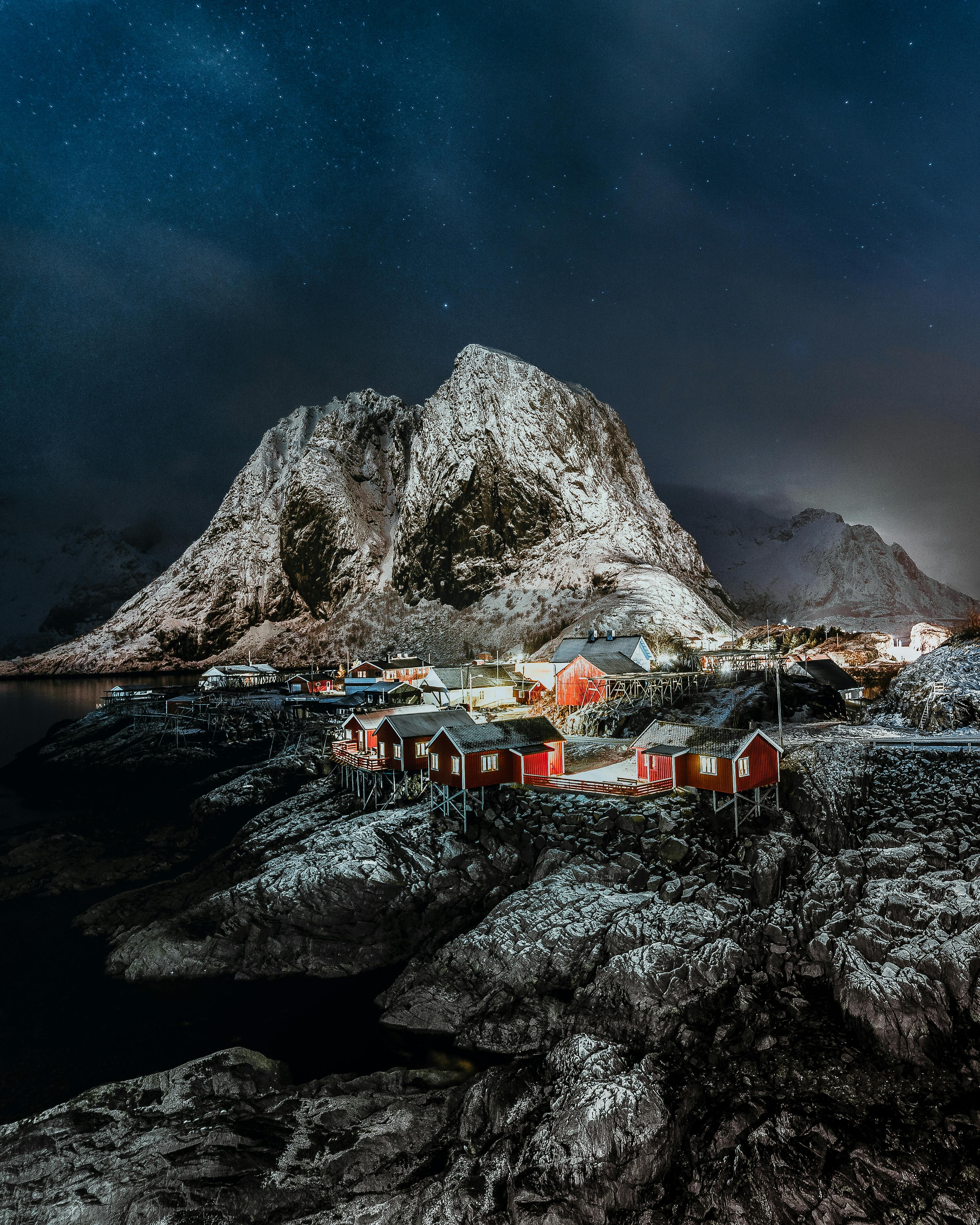 Picturesque scenery of small settlement with glowing lights located near calm lake and mountains