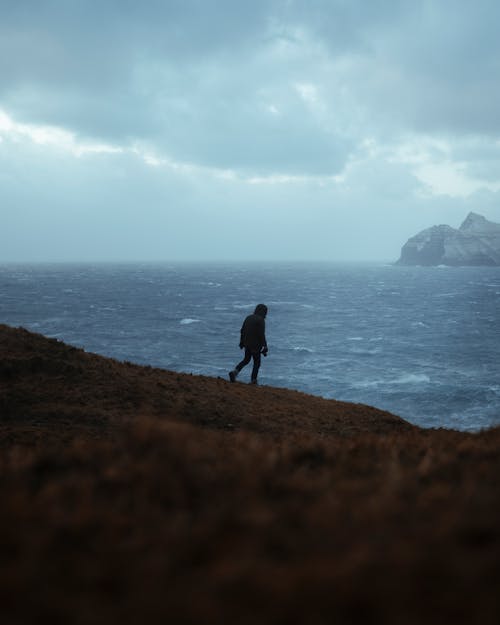 Человек, стоящий на коричневой скале возле водоема