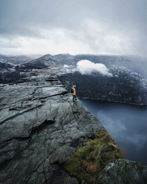 Человек в черном пиджаке стоит на скале возле озера