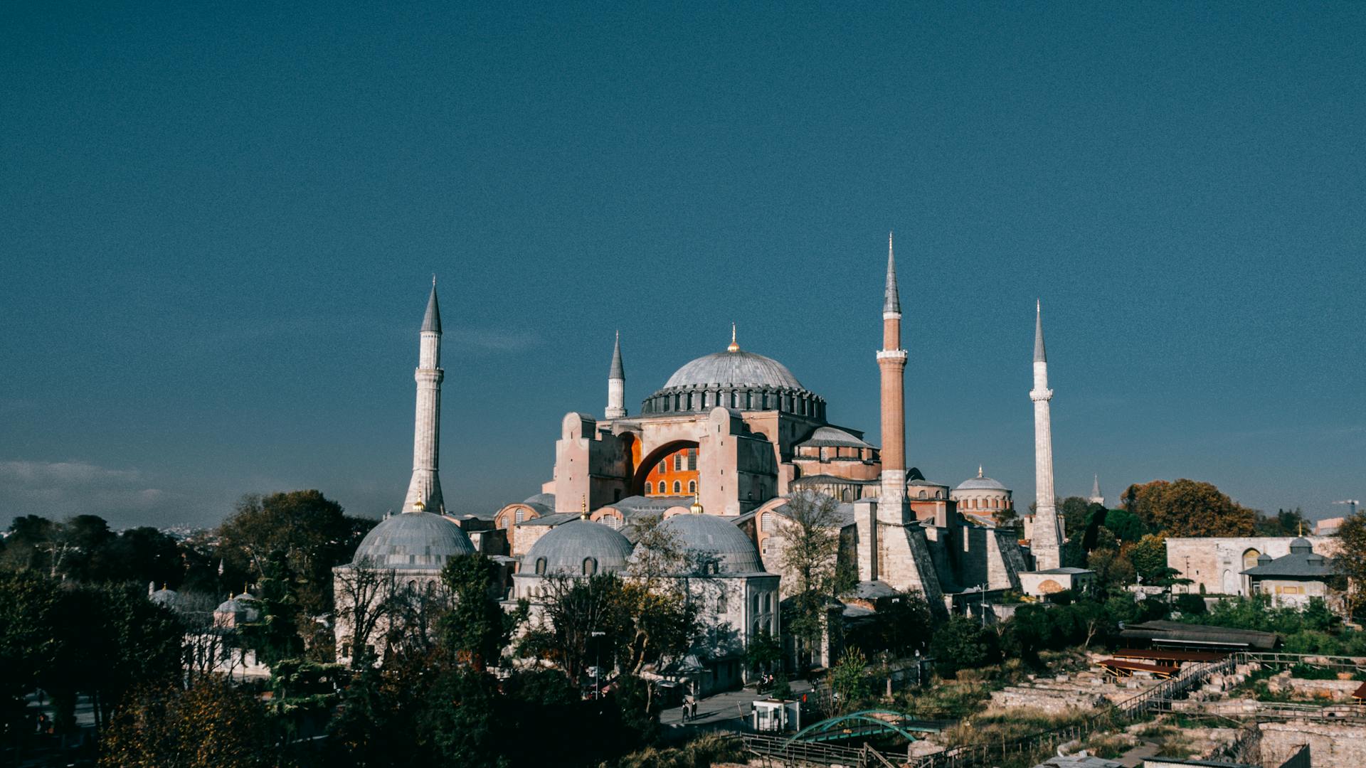 Famous Hagia Sophia grand mosque with high minarets and dome located among green trees in Turkey against blue sky in city