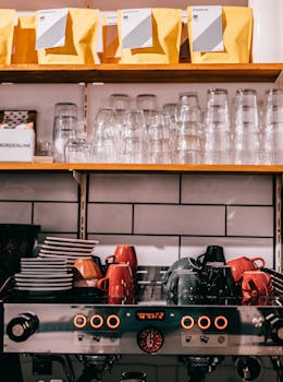 Professional coffee maker with cups and saucers under transparent glasses and row of packages in cafeteria kitchen