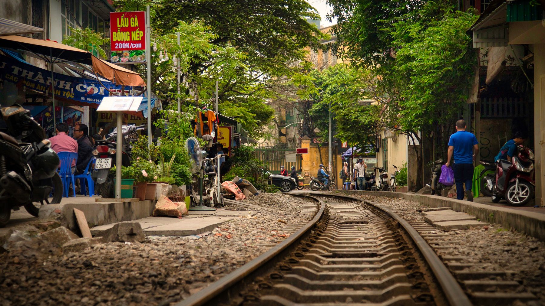 Vibrant Hanoi street scene with urban train tracks and daily life unfolding nearby.