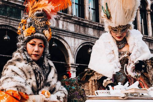 Free Two women in elaborate Venetian costumes enjoying a tea party during a masquerade festival. Stock Photo