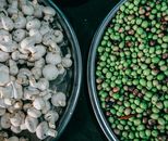 Top view composition of ripe raw green peas and fresh mushrooms heaped in steel bowls and placed on dark table