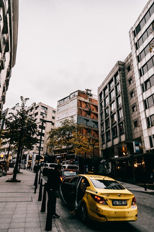 Narrow contemporary city street with parked yellow taxi between modern residential buildings under cloudy sky