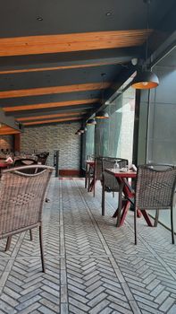 Stylish indoor dining area featuring wicker chairs, wooden beams, and large windows for natural light.