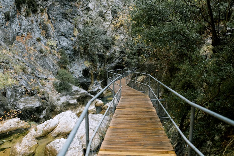 Small Footbridge Over River In Mountainous Terrain