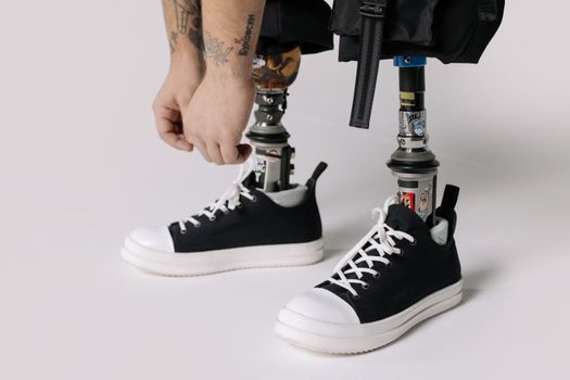 Close-up of a man tying shoelaces on sneakers attached to prosthetic legs.