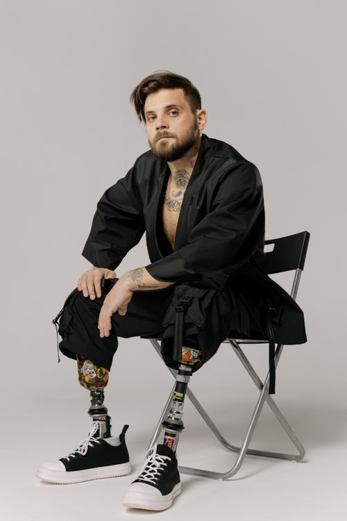 Free Bearded man with prosthetic legs sitting confidently on chair in studio. Empowerment and strength. Stock Photo