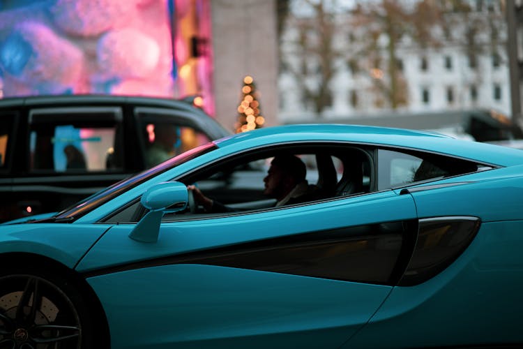 A Man Driving A Blue Mclaren Supercar