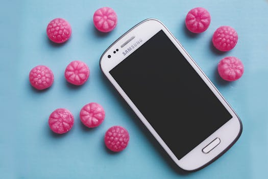 White smartphone surrounded by pink candy on a blue background, creating a vibrant flat lay.