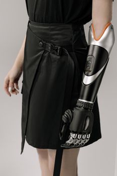 Close-up of a woman with a modern prosthetic arm wearing a black skirt in a studio shot.