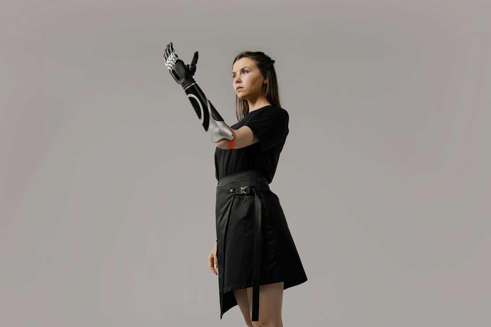Empowering portrait of a young woman showcasing a futuristic prosthetic arm in a studio setting.