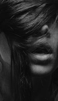 Dramatic black and white portrait of a woman with mouth slightly open and hair covering her face.