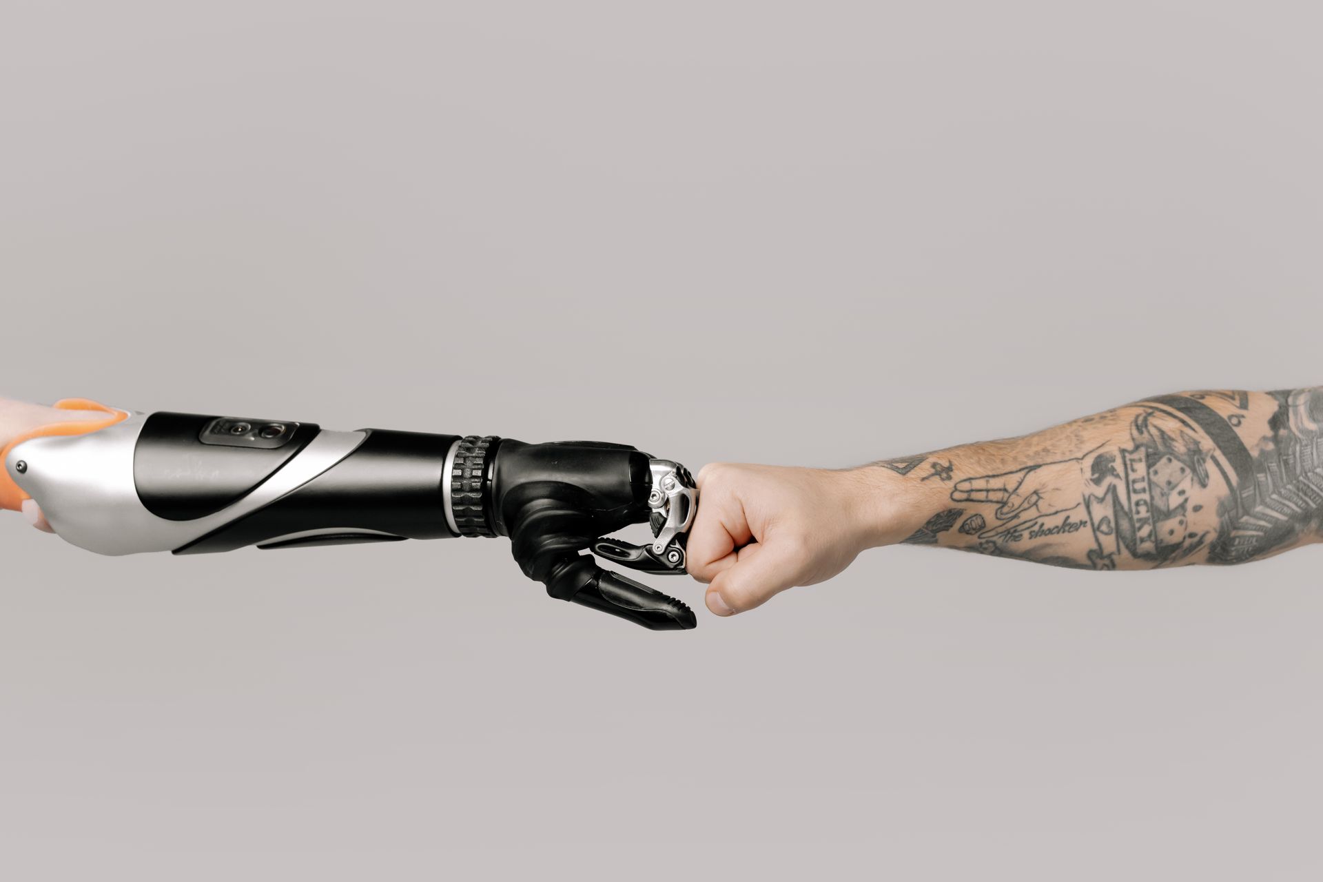 Close-up of a tattooed arm fist bumping with a robotic prosthetic arm in studio setting.