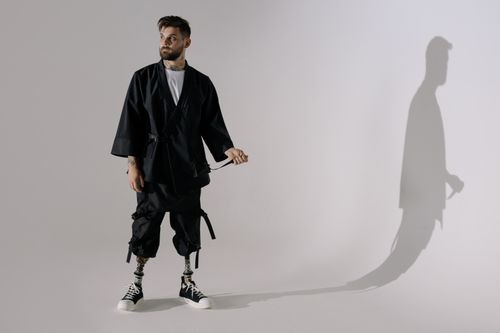 Free A modern, stylish man with prosthetic legs wears black clothing and sneakers in a studio setting. Stock Photo