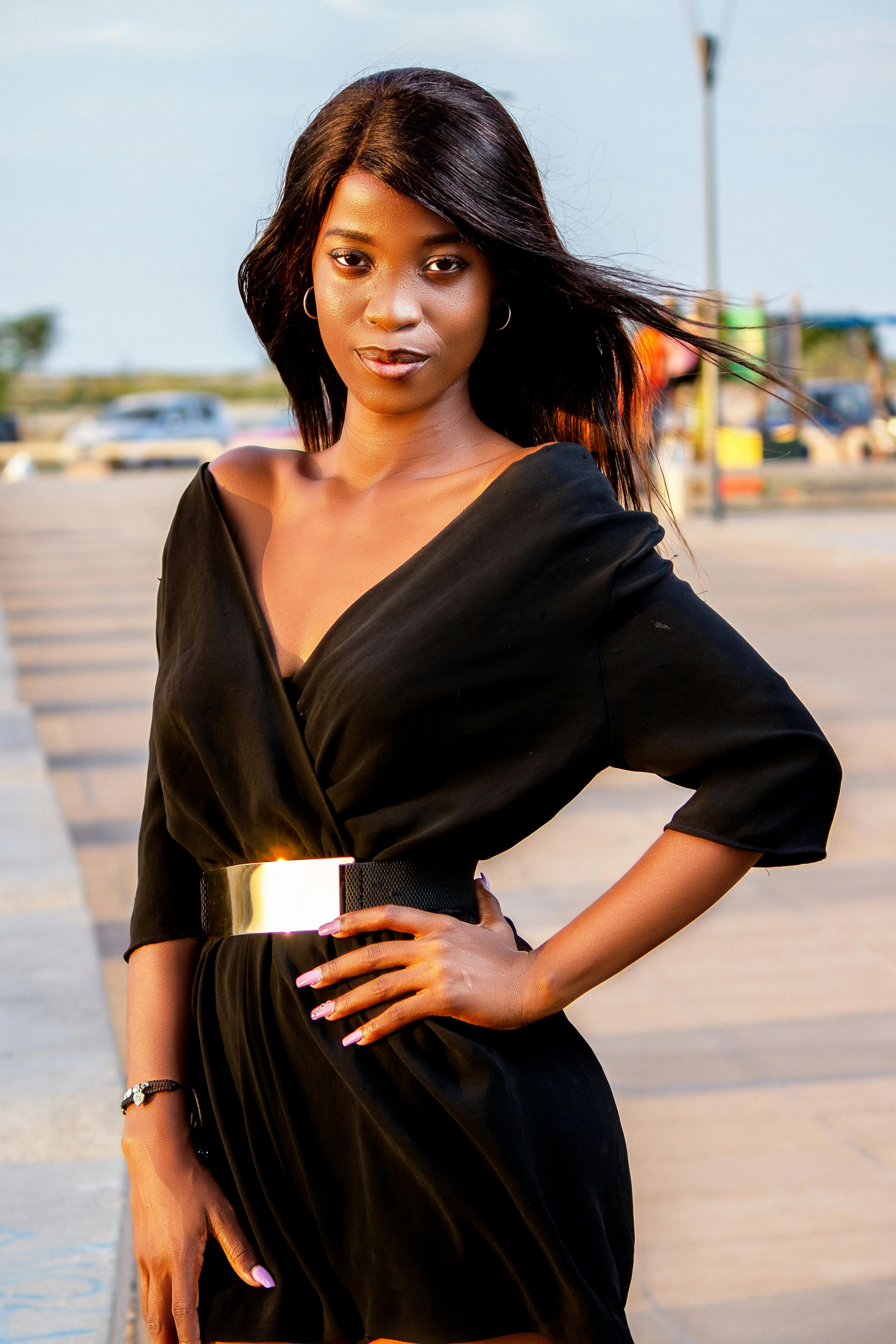 Free Stylish woman in black dress posing confidently outdoors on a sunny day. Stock Photo