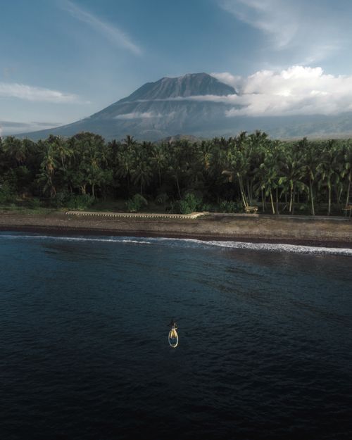 Free Paddleboarder exploring a tranquil tropical shoreline with a majestic mountain view. Stock Photo