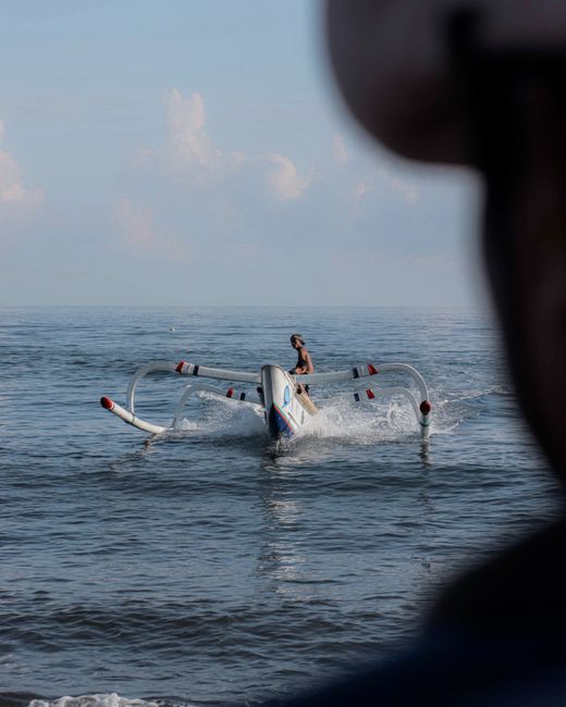 Person in boat with outriggers on sides floating on rippling pure turquoise sea water surface