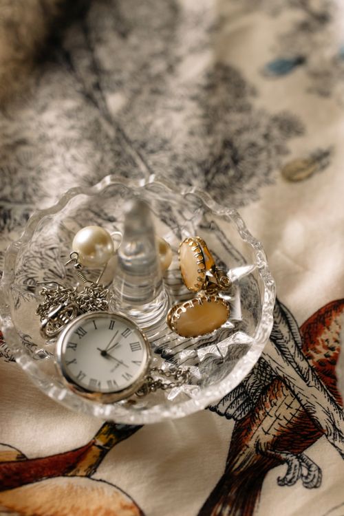 Free A beautiful display of jewelry and a pocket watch in a crystal dish on a patterned fabric. Stock Photo