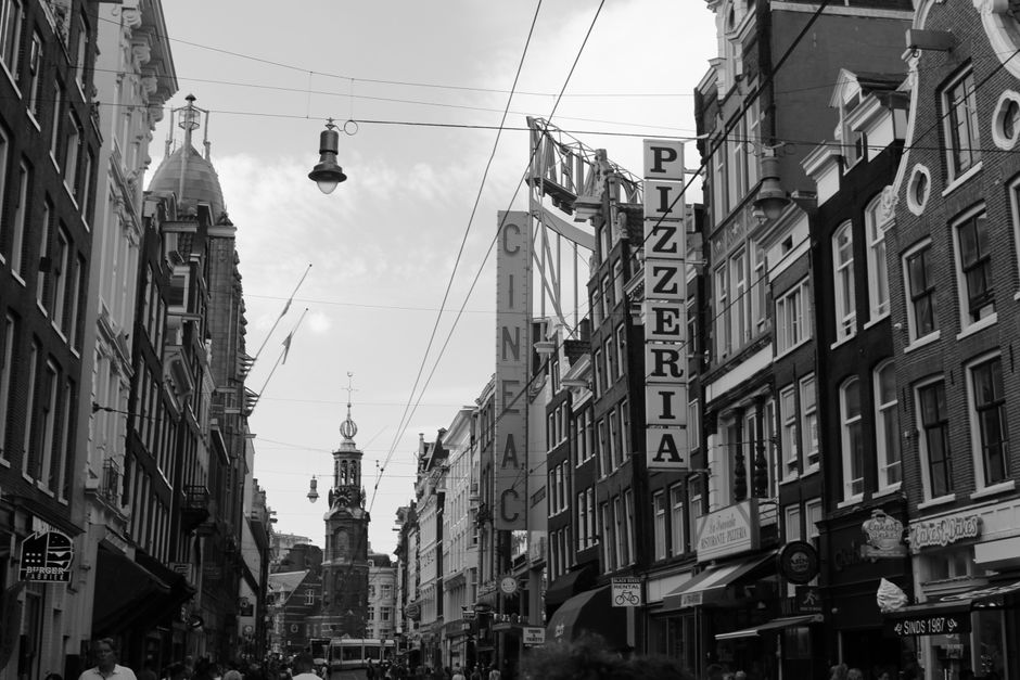 Black and white street scene in Amsterdam with signage and historic buildings.