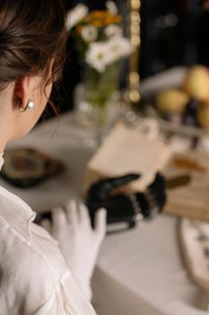 A woman examines a robotic hand in an art studio, surrounded by creative supplies.