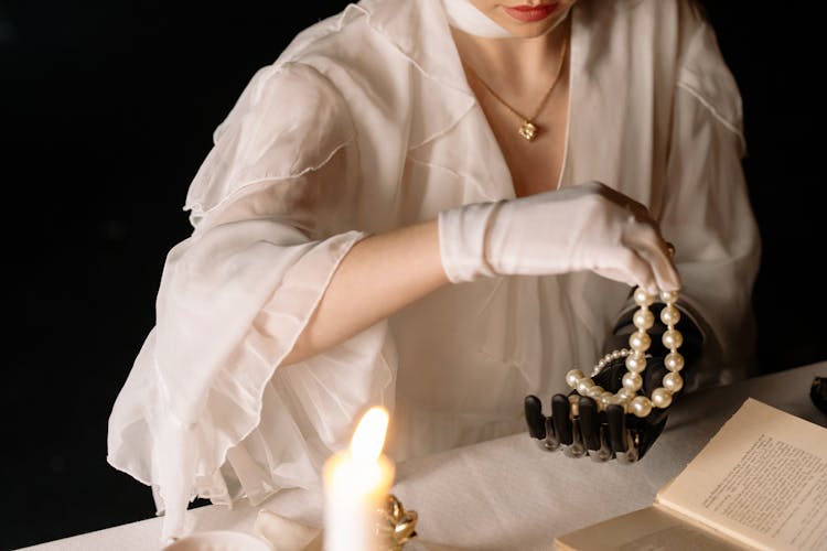 Person In Off White Dress With White Gloves Holding A Pearl Necklace