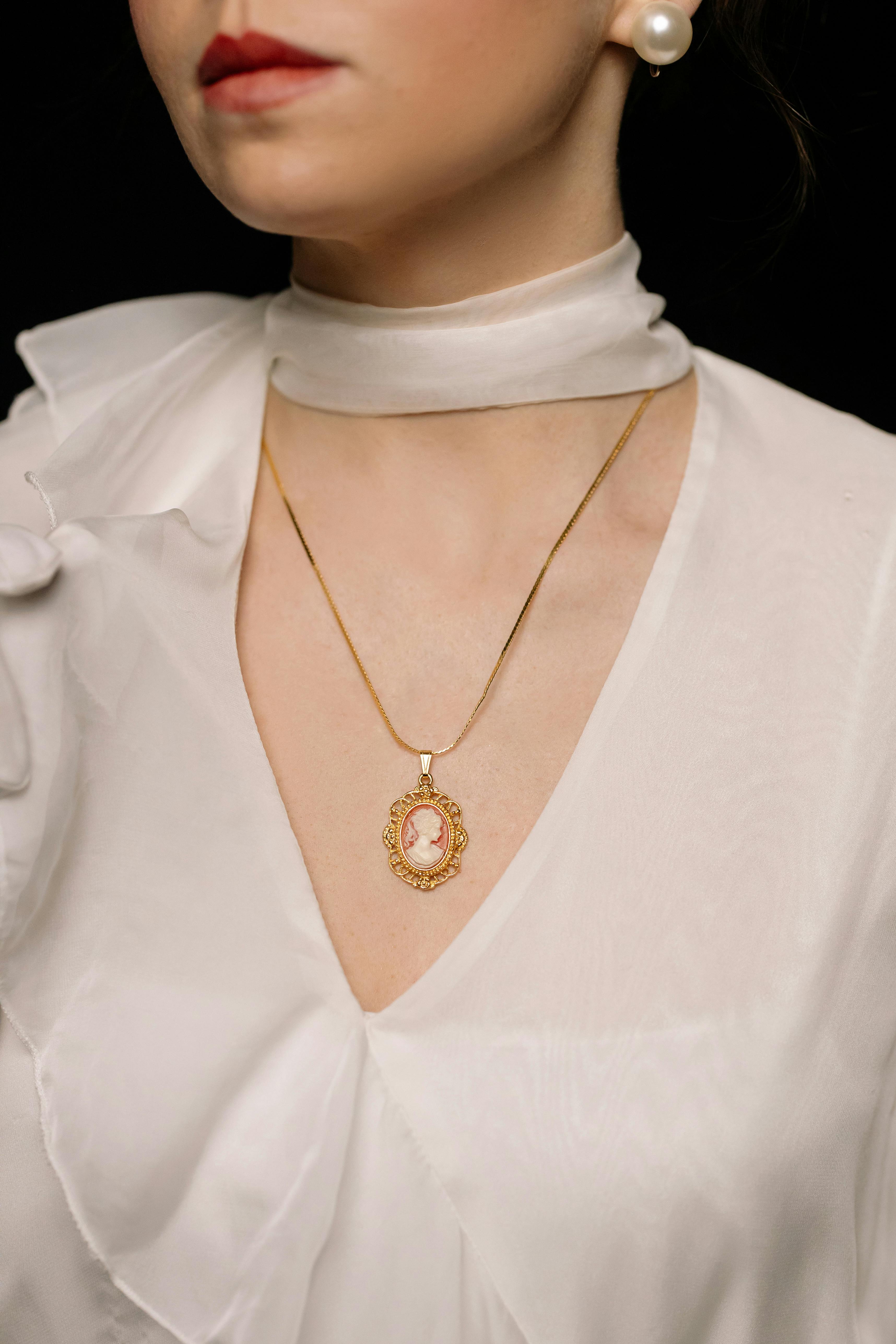 woman in white top wearing gold necklace with pendant