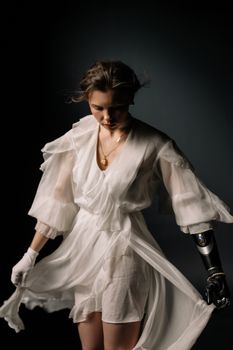 A woman with a prosthetic arm wearing a flowing white dress and gold necklace.