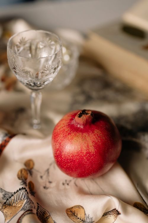 Free A vibrant pomegranate next to a crystal glass on a decorative cloth, set in a warm and inviting atmosphere. Stock Photo