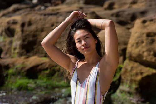 Free Woman in striped swimsuit posing by rocky shore, enjoying the sunny day. Stock Photo