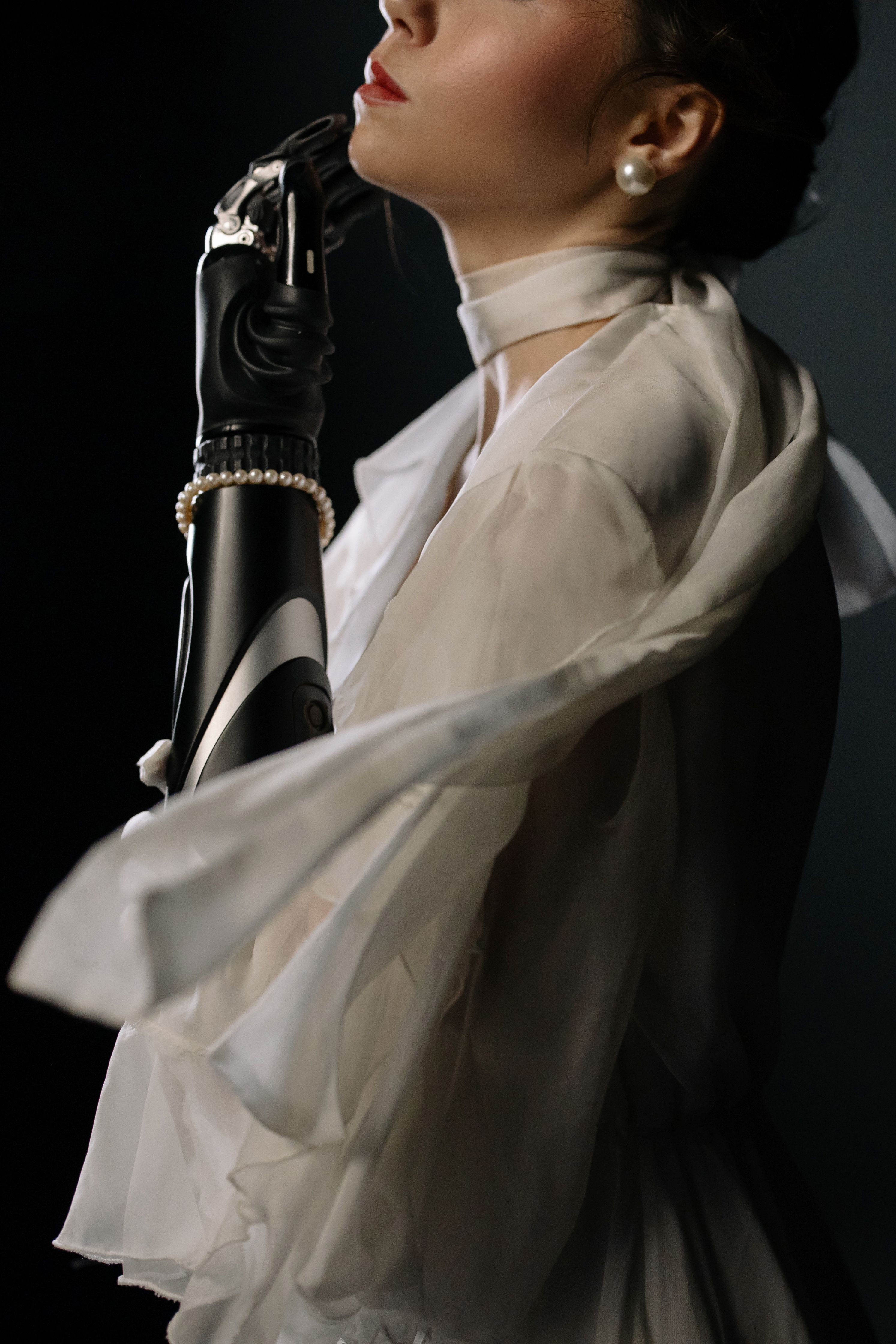 A portrait of an elegant woman with a futuristic prosthetic arm and flowing white dress.