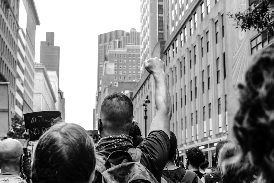 Free Black and white back view of crop anonymous activists with fist up fighting for social rights between urban buildings Stock Photo