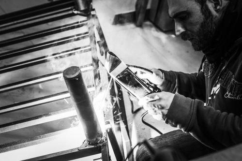 Free Black and white image of a man welding metal, showcasing focus and craftsmanship. Stock Photo