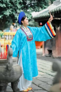 A woman wearing a vibrant blue traditional dress stands outdoors, engaging with cultural rituals.